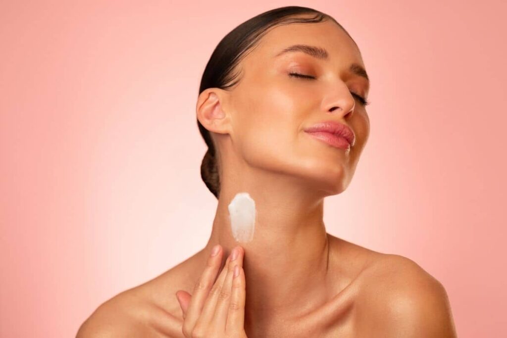 Young woman gently applying cream to her neck, focusing on post-neck lift skincare for smooth recovery.