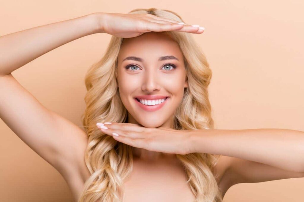 Smiling blonde woman framing her face with hands, showcasing natural results of Baby Botox treatment.