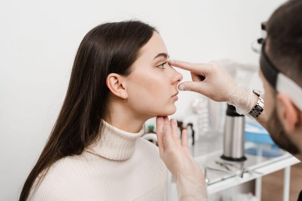 Doctor examining a patient's nose during a consultation for revision rhinoplasty to address a bulbous tip.