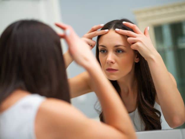 Woman examining her forehead in the mirror, checking for wrinkles and potential natural treatments.