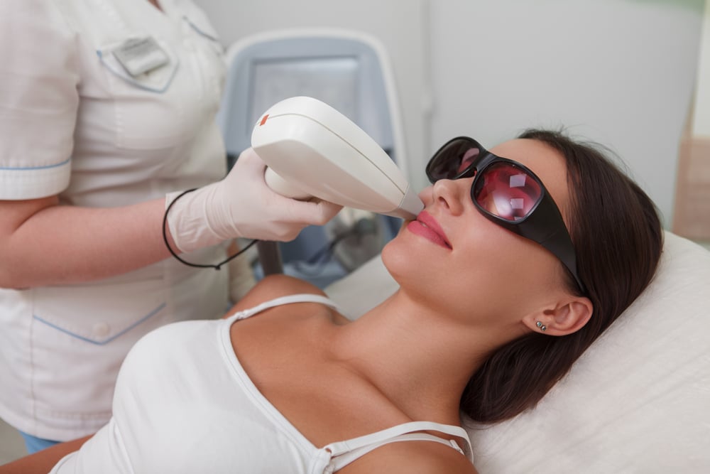Woman receiving laser treatment on her upper lip while wearing protective eyewear at a cosmetic clinic.