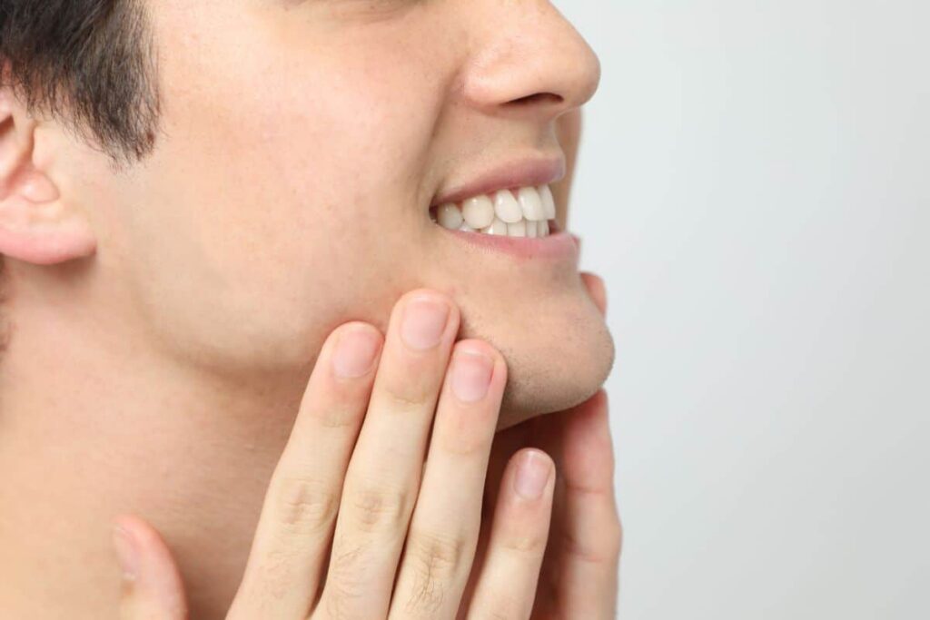 Close-up of a man touching his defined jawline, showcasing results of chin implants and neck liposuction.