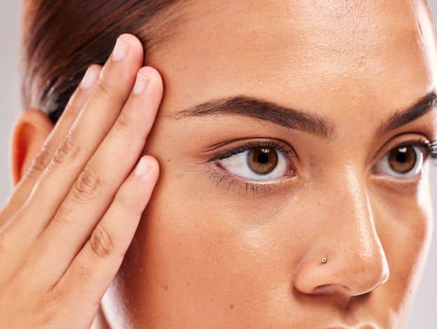 Close-up of a woman touching her temple, highlighting skin texture and treatments for crow’s feet.
