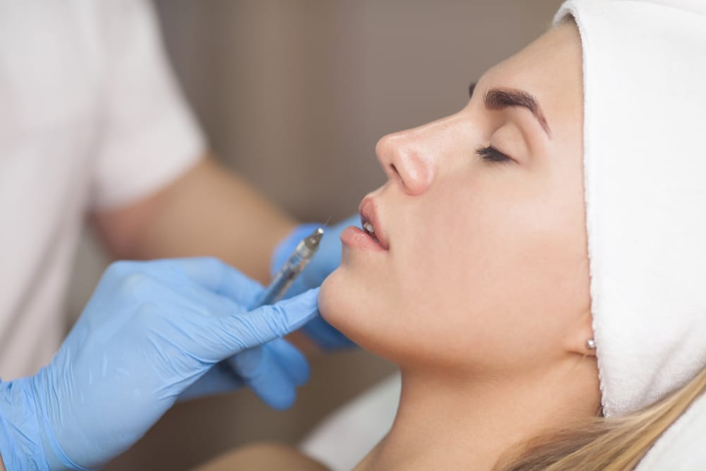 Woman receiving a PRF injection in her lips from a professional wearing blue gloves in a medical setting.
