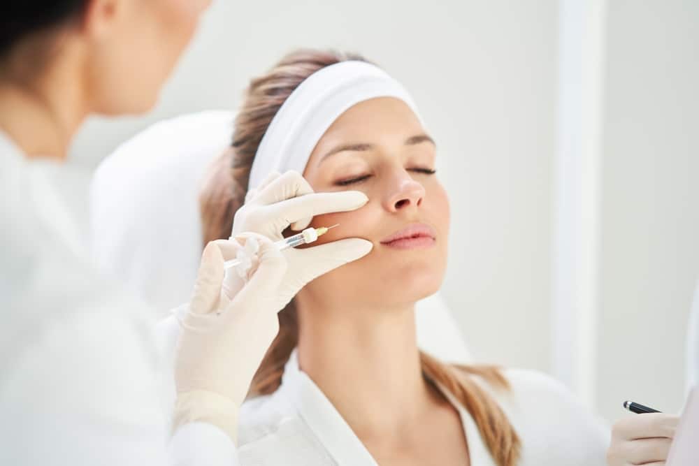 Woman receiving a steroid injection on her cheek from a professional wearing white gloves in a medical clinic.
