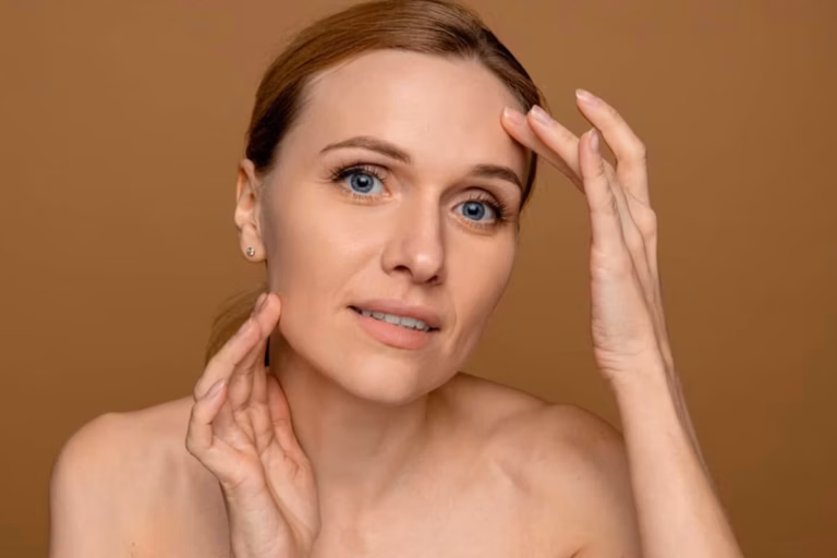 A woman gently lifting the skin around her temple and jawline with her fingers to simulate the results of a facial lifting procedure.
